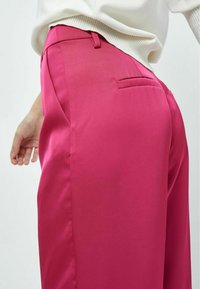 Fuchsia trousers with a smooth, satin texture, featuring a side pocket and a tailored fit. The waistband has belt loops for adjustable sizing.