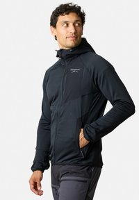 Zwarte zip-up jack met een getailleerd ontwerp, voorzien van een capuchon, zijzakken en textiel met structuur. Logo op de borst, soepel en rekbaar materiaal.