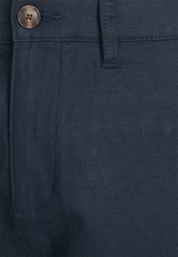 Mörkblå byxor med linnestruktur, utrustade med knappstängning och sidofickor. Tyget verkar lätt och andningsbart.