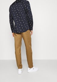 Una camicia blu navy con stampa floreale, abbinata a pantaloni beige e sneakers bianche, che mostrano un look casual e moderno.