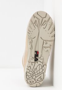 Suola di sneaker color beige chiaro con schemi testurizzati e un logo in nero e rosso, caratterizzata da una suola spessa e robusta per una migliore trazione.