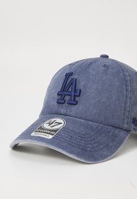 Marineblå baseballcap med et broderet "LA" logo på forsiden. Har en buet skygge og et mærke, der angiver regulerbar pasform.