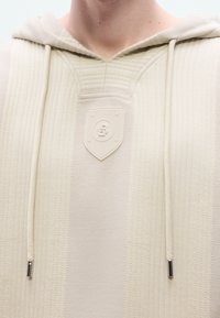 Μπεζ φούτερ με κουκούλα και υφασμάτινο σχέδιο, με ραμμένη λογότυπη ετικέτα στο μπροστινό μέρος, κορδόνια και δομημένη κουκούλα.