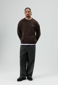 Bruine trui met "RACER'S VIBE" borduursel, gecombineerd met loszittende donkergrijze spijkerbroek en zwarte schoenen met roze veters. Eenvoudig, ontspannen ontwerp.