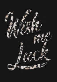 Černá látka zdobená vyšívaným nápisem "Přej mi štěstí" v leopardím vzoru s jemnou texturou, lemovaná černým stehem.