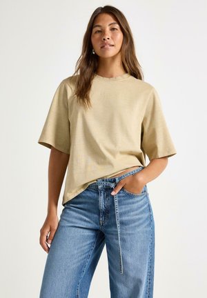 Beige t-shirt med kort ärm och rund halsringning, avslappnad passform, matchad med ljusblå högmidjade jeans med rak ben och framficka.