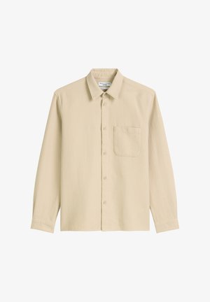 Chemise beige à manches longues en tissu texturé, avec un col, des boutons à l'avant et une poche sur la poitrine.
