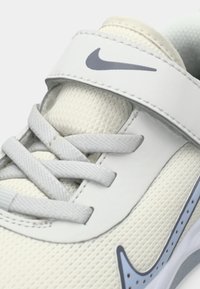 Baskets de sport Nike en crème clair et gris. Présentent un dessus en maille texturée, des lacets gris plats et une sangle à crochets et boucles avec un logo.