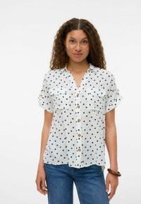Chemise blanche à manches courtes avec des pois noirs, avec un col boutonné à l'avant et deux poches sur la poitrine. Tissu doux avec une coupe décontractée.