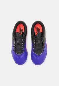 Des chaussures de sport violettes avec un dessus texturé, des lacets noirs et des accents orange sur les semelles intérieures. Elles sont dotées d'un design épuré pour offrir un bon maintien.