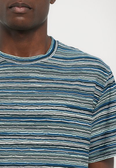 T-shirt à manches courtes rayé en bleu, vert et gris avec un motif de vagues texturé et un col rond. Le matériau semble doux et léger.