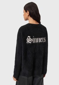 Musta pörröinen neule, löysällä istuvuudella, jossa takana valkoisella teksti "Sinners". Pehmeä rakenne ja pyöreä pääntie.