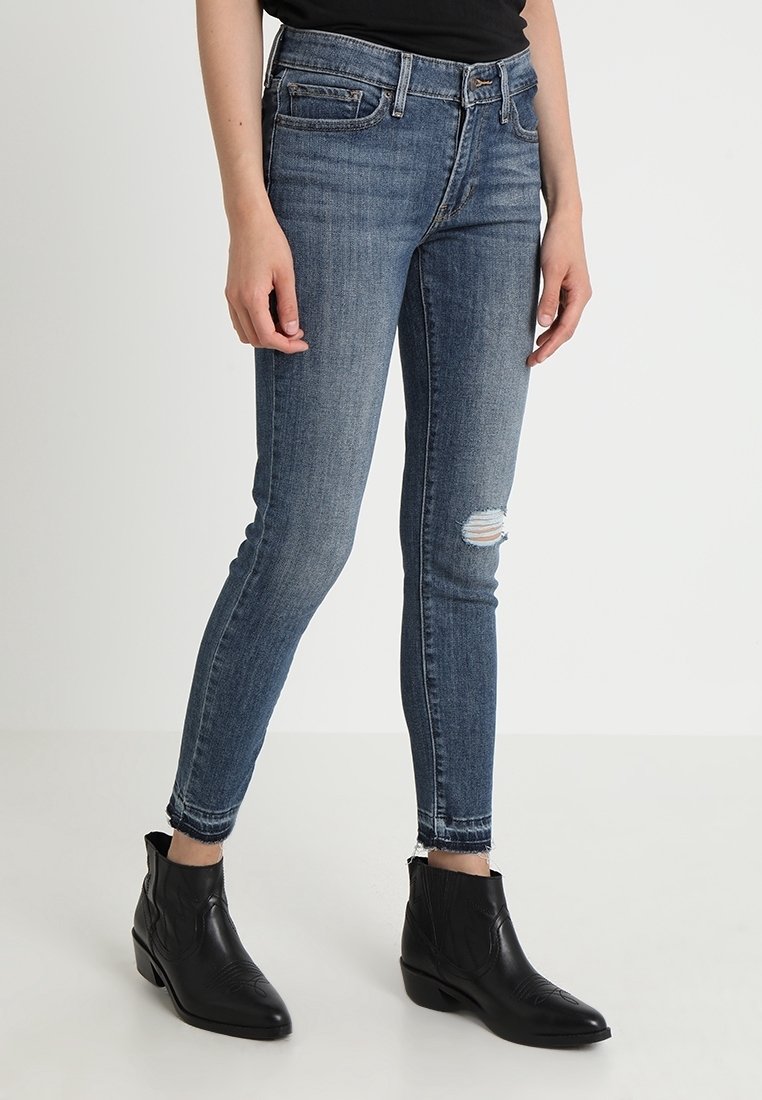 Jeans ajustados en denim azul oscuro con detalle de rodillas desgastadas. Cuenta con cinco bolsillos y un dobladillo deshilachado en el tobillo. Combinados con botas negras de tobillo.