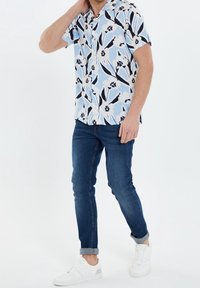 Kurzärmeliges Hemd in Hellblau mit einem floralen Muster in Schwarz und Weiß. Tragen mit dunkelblauen Jeans und weißen Sneakers.