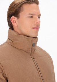 Bruine gewatteerde jas met een hoge kraag, voorzien van een centrale ritssluiting, horizontale quiltstructuur en een slank, lichtgewicht ontwerp.