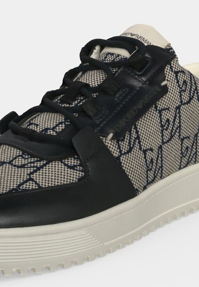 Gros plan d'une basket à motifs avec des accents en cuir noir, des lacets noirs et une semelle blanche dotée d'une adhérence texturée.