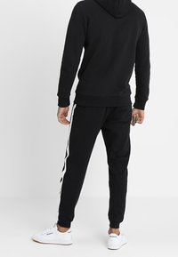 Black sweatshirt with a hood, paired with black joggers featuring white side stripes. Material looks soft; fit appears relaxed.