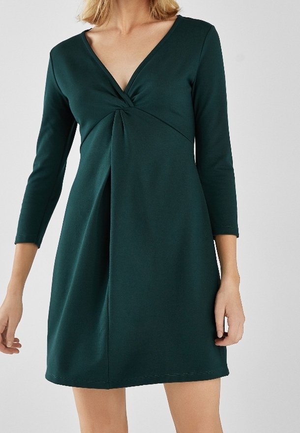 Robe verte à manches longues avec un décolleté en V et un détail torsadé au niveau de la poitrine. Fabriquée en tissu doux et extensible, avec une silhouette évasée.