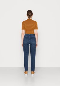 Camiseta de mostaza a rayas con mangas cortas, combinada con unos jeans de talle alto de color azul oscuro y zapatos de lienzo color beige, vista desde la parte de atrás.