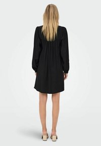 Czarna sukienka z długimi bufkami, zebranym detalem na plecach i luźnym krojem, sięgająca do połowy uda. Gładka faktura i minimalistyczny design.