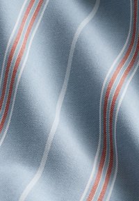 Textil mit hellblauem Hintergrund und wellenförmigen roten und weißen Streifen. Der Stoff wirkt strukturiert mit einem gewebten Muster.