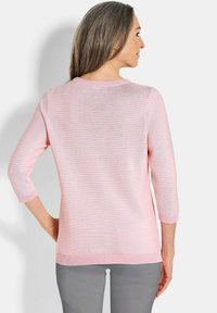 Hellrosa gestreifter Pullover mit drei Viertelärmeln, geripptem Ausschnitt und Saum. Weiche Textur, lässige Passform, kombiniert mit grauen Hosen.
