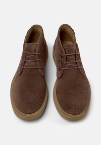 Scarpe in suede marrone con punta rotonda, caratterizzate da una superficie liscia, design con lacci e una suola in gomma robusta. Stile classico e minimalista.