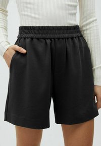 Zwarte, ontspannen shorts met een elastische tailleband en zijzakken, gemaakt van een zachte stof met een gladde textuur.
