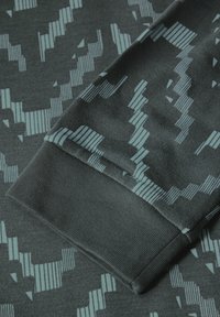 Tissu gris avec un motif texturé présentant des lignes verticales et horizontales bleu clair. Le poignet est replié, montrant une finition lisse.