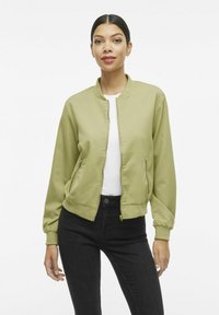 Giacca bomber color khaki realizzata in tessuto liscio, con zip frontale, polsini a costine, due tasche laterali e un design corto.