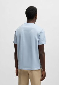 Helleblaue, kurzärmelige T-Shirt aus strukturierter Baumwolle, mit Rundhalsausschnitt und seitlichen Schlitzen für Bewegungsfreiheit. Rücken hat ein kleines Detail.