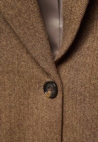 Veste en laine marron à chevrons avec col cranté et fermeture par un bouton marron foncé à quatre trous.
