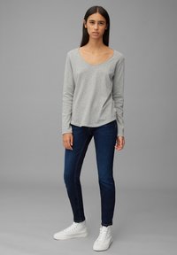 Grå langermet T-skjorte med V-hals, kombinert med mørk denim jeans og hvite høyhælte sneakers, vist mot en nøytral bakgrunn.
