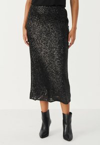 Jupe midi en sequins noirs avec une taille ajustée, une texture chatoyante et une coupe droite, associée à des bottines noires.