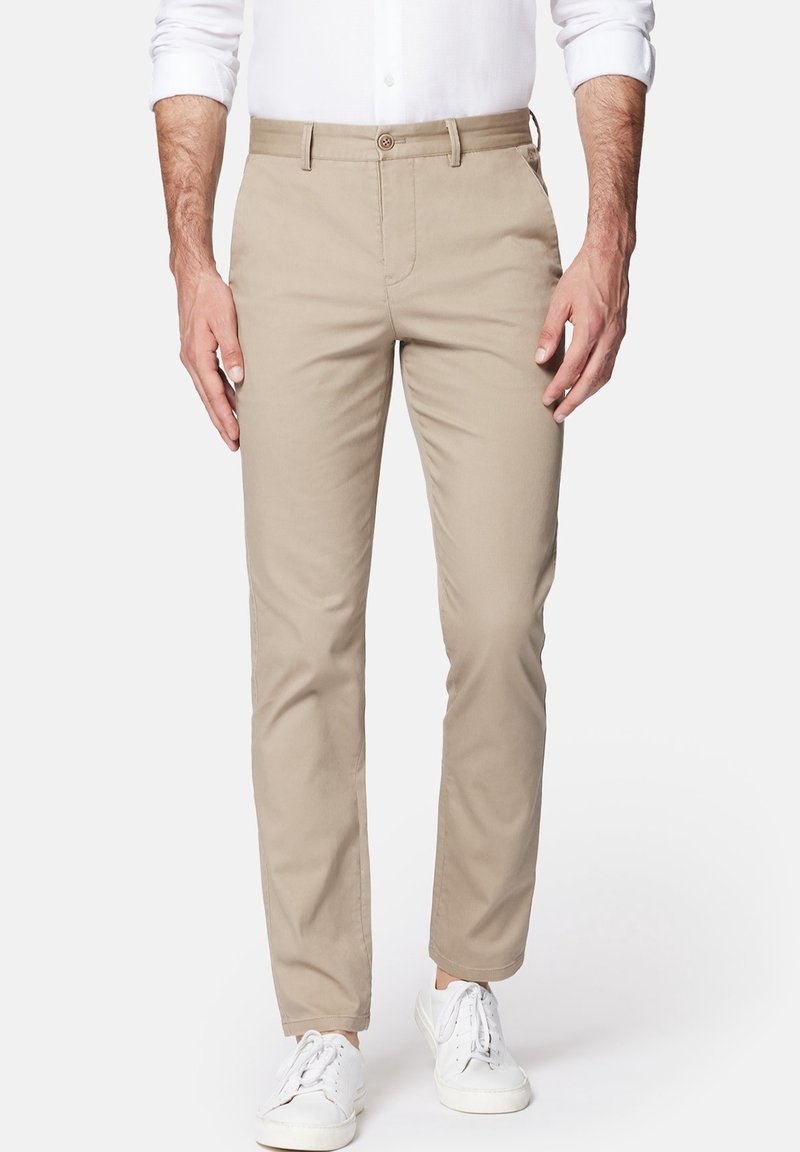 Bežové bavlněné kalhoty s rovný fit, obsahující boční kapsy, přední zapínání na knoflík a hladký povrch. Nosené s bílými teniskami.