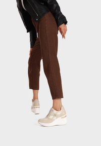 Sneaker platform beige con suole bianche, dettagli in suede e particolari dorati. Indossate con pantaloni cropped marroni e una giacca di pelle nera.