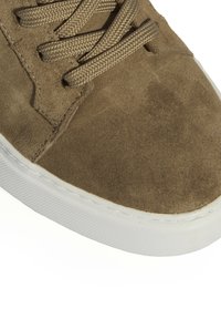 Baskets en suede marron avec lacets plats en tissu tissé et semelle en caoutchouc blanc. Présente une texture lisse et des coutures le long des bords de la chaussure.