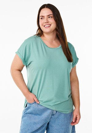 Lys grøn kortærmet t-shirt med rund halsudskæring og opsmøg på ærmerne, parret med lyseblå denimshorts. Blød, glat stoftekstur.