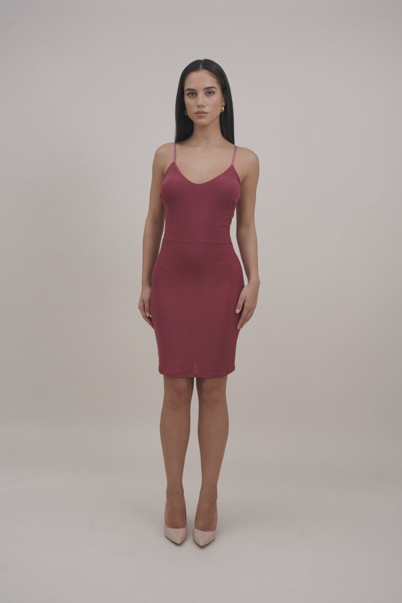 Εφαρμοστό, μήκους γόνατος φόρεμα σε λαμπερό μπορντό με λεπτές τιράντες και βαθύ V-ντεκολτέ, συνδυασμένο με γυμνές ψηλές γόβες.