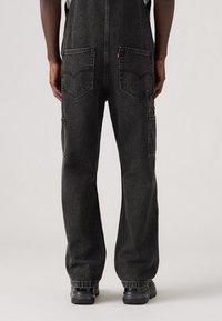 Svarta denimoveraller med avslappnad passform, som har två bakfickor och en sidficka, i kombination med svarta strukturerade skor.