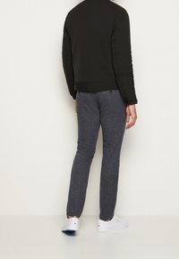 Zwarte gewatteerde jas met doorstikte schouders, gecombineerd met donkergrijze joggingbroek. Witte sneakers maken de outfit compleet.