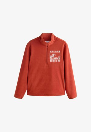 Fényes narancssárga polár pulóver, magas gallérral és fél cipzárral az elején. Fehér grafikával díszített a mellrészen. Simább tapintású anyag.