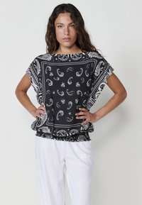 Blouse noire avec des motifs cachemire et floraux blancs, manches courtes et ourlet froncé. Assortie à un pantalon léger blanc.