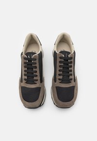 Joggesko med en svart mesh-overdel, taupe suede-detaljer, beige detaljer og svarte snorer. Rund tå og polstret såle.