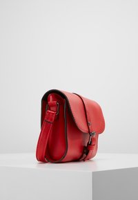 Czerwona skórzana torebka crossbody z klapą, czarnymi wykończeniami i regulowanym paskiem. Gładka tekstura z subtelnymi detalami przeszyć.