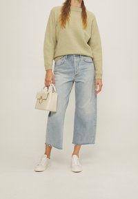 Ljusgrön stickad tröja, ljusblå vida jeans med fransar vid bensluten, vita sneakers och en liten krämfärgad handväska med guldaccent.