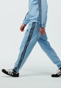 Light blue tracksuit with black stripes, featuring a zip-up jacket and matching pants, complemented by black and white sneakers.