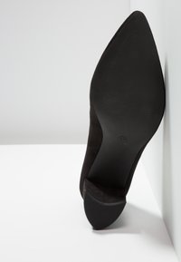 Chaussure à talon haut en daim noir avec un bout pointu. La semelle en caoutchouc comporte un motif antidérapant texturé. Taille 37 indiquée sur la semelle.