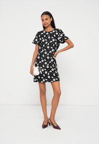 Čierne kvetinové šaty s krátkymi rukávmi, výstrihom s otvorom a bielym kvetinovým vzorom. Kombinované s malou bielou kabelkou a bordovými lodičkami.