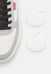 Levi's sneakerissä valkoista ja harmaata nahkaa mustilla nauhoilla. Mukana on kaksi valkoista pyöreää nauhaa, teksturoitu yläosa, jossa on reikiä.